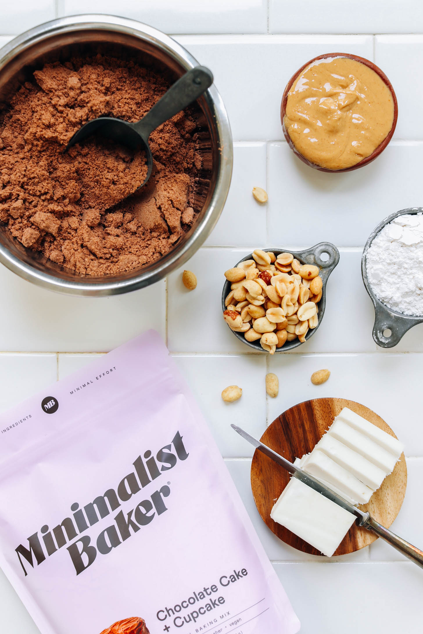 Tüte und Schale unserer glutenfreien Schokoladenkuchenmischung neben Erdnussbutter, Erdnüssen, Puderzucker und veganer Butter