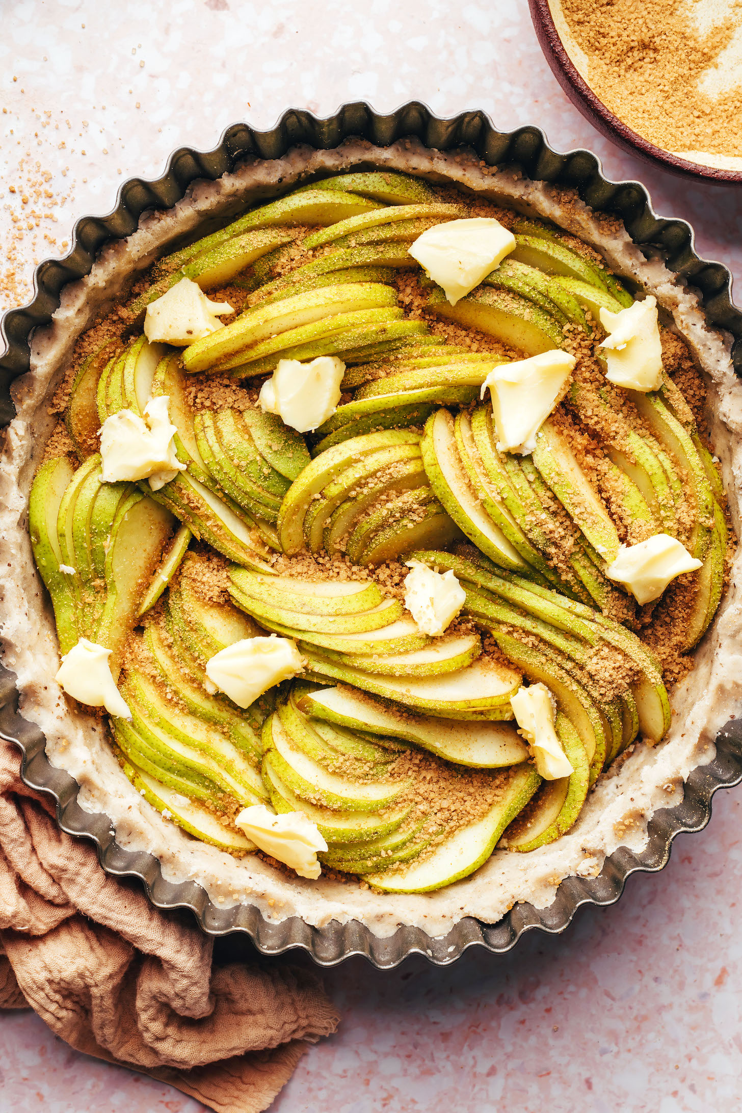 Sliced ​​pears, vegan butter and brown sugar over a crust in a pie tin
