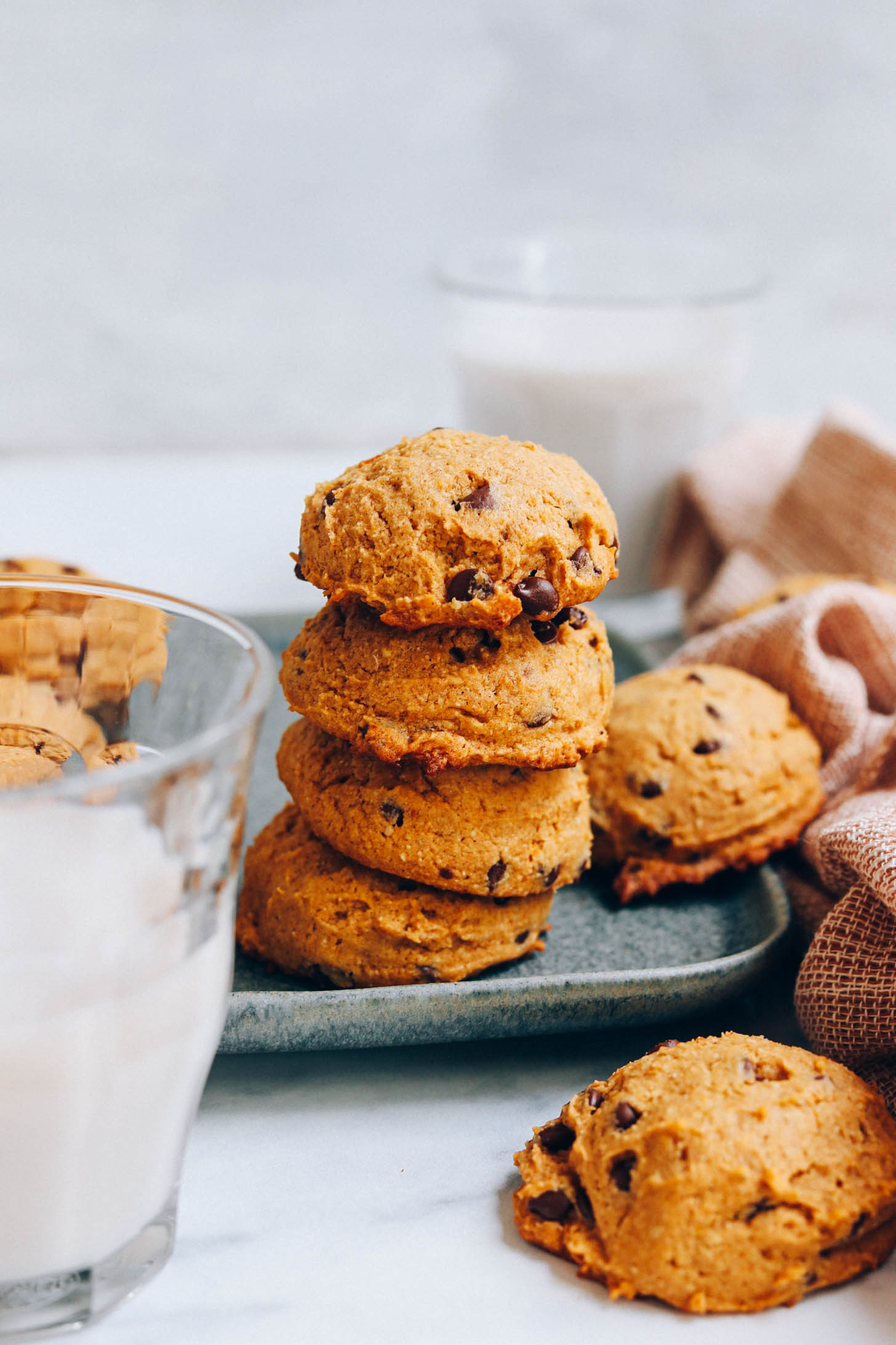 Stack of pumpkin chocolate chip cookies on a tray next to glasses of dairy-free milk