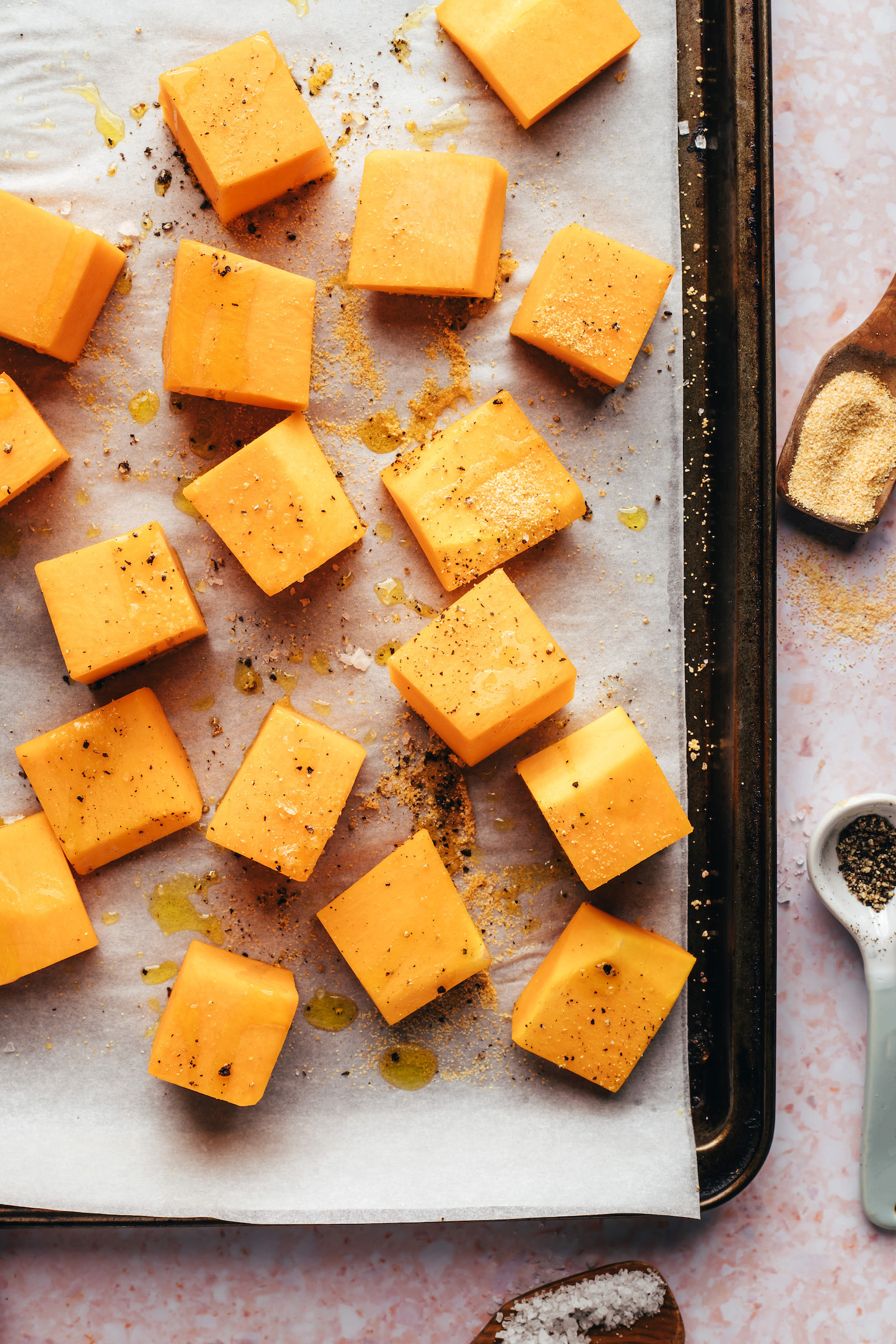 Cubed butternut squash on a baking sheet drizzled with oil and sprinkled with seasonings