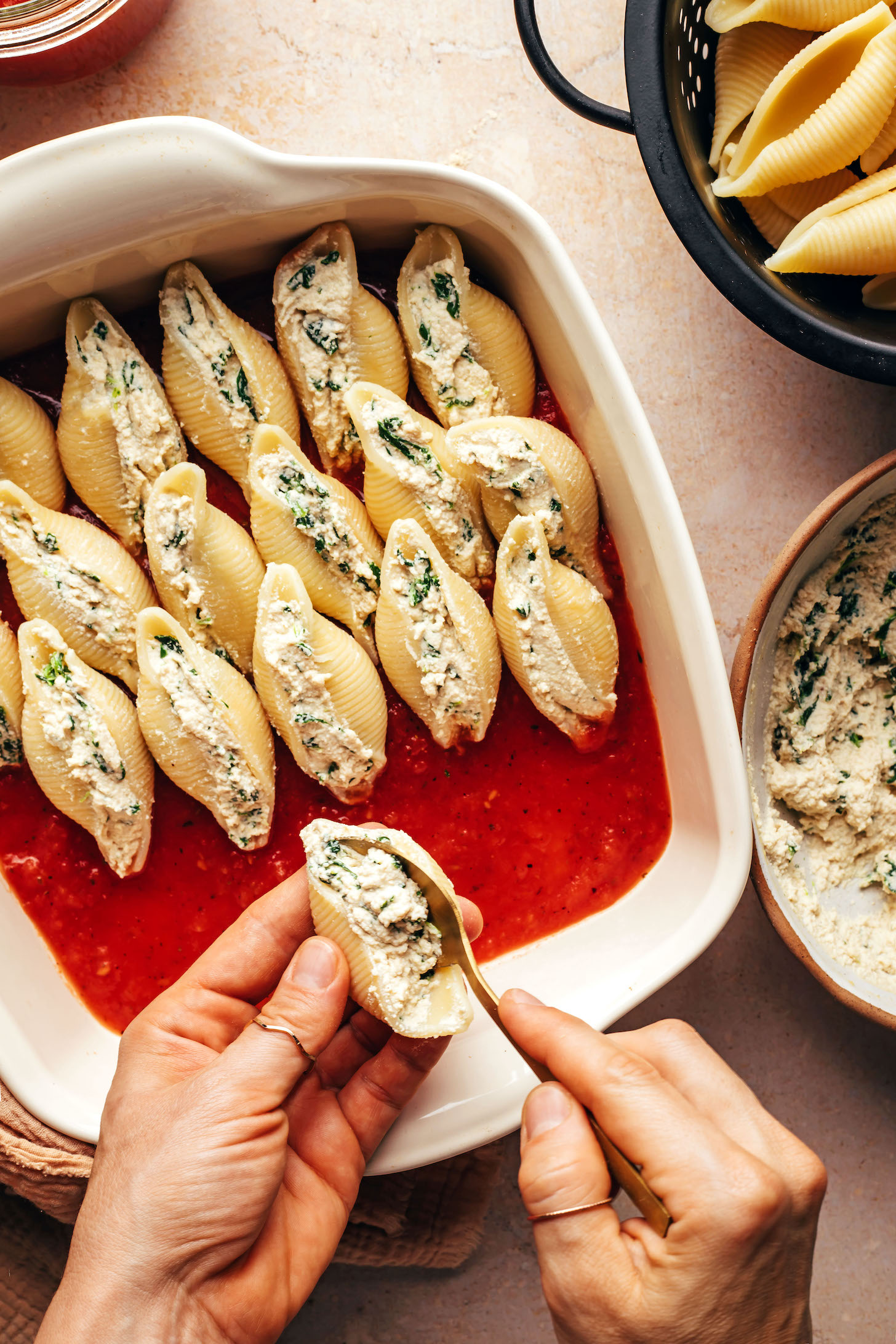 Using a spoon to add a tofu, cashew, and spinach filling to pasta shells
