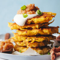 Stack of vegan gluten-free latkes topped with dairy-free sour cream, applesauce, and green onion