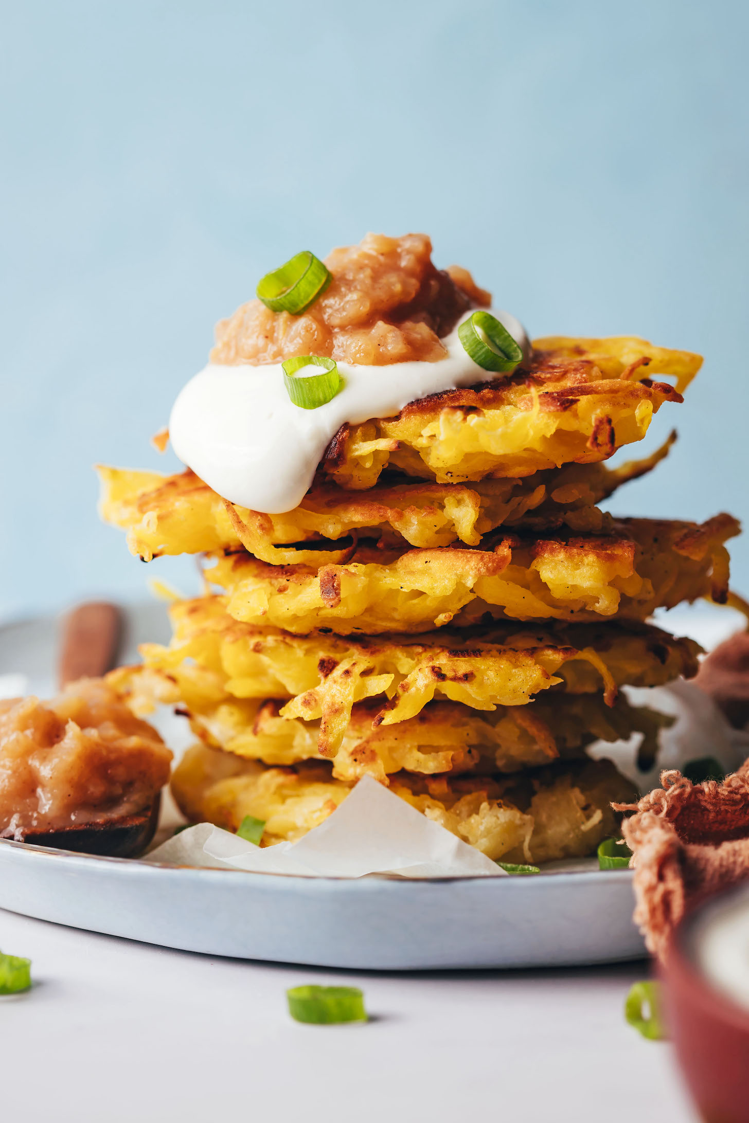 Stack of crispy latkes topped with vegan sour cream, applesauce, and green onions