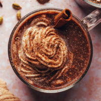 Overhead shot of a mug of chai hot chocolate with coconut whipped cream and a cinnamon stick as a straw