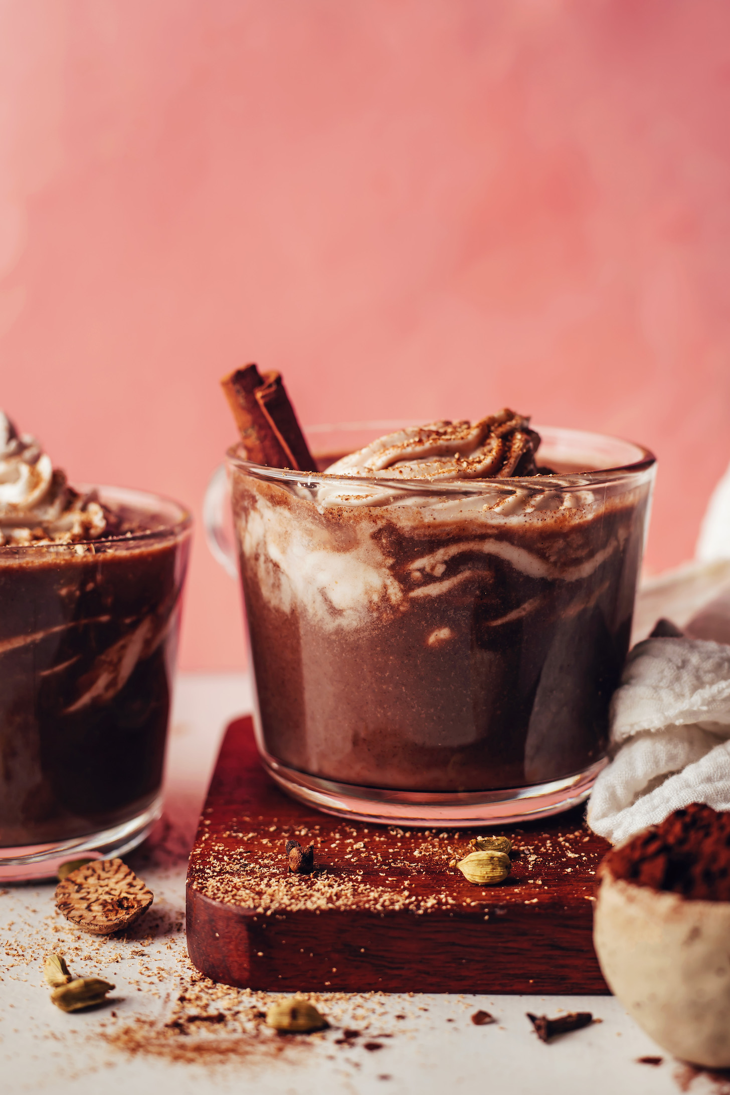 Vista lateral de dos tazas de chocolate caliente sin lácteos cubierto con crema batida de coco y especias chai