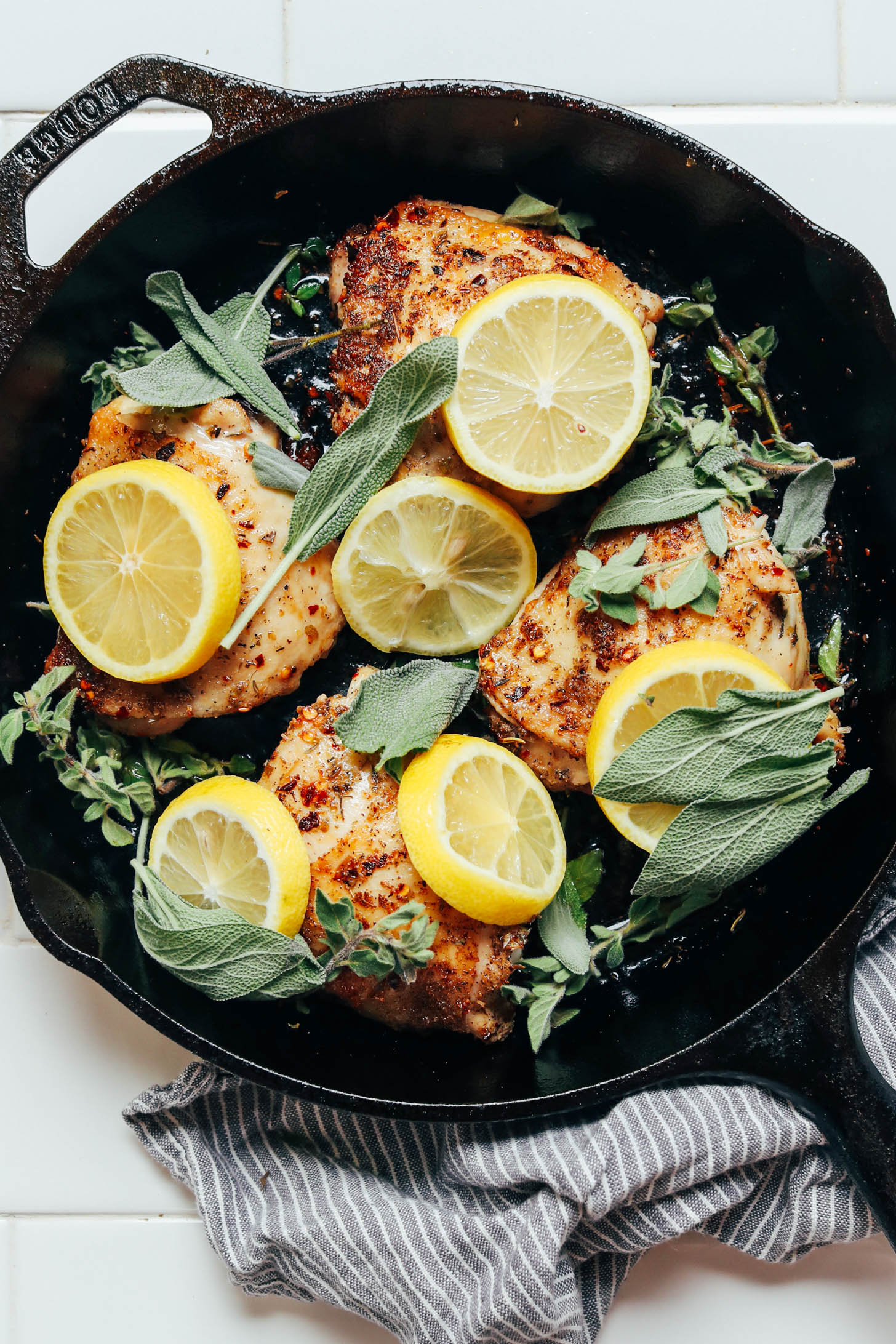 Skillet of seared chicken thighs garnished with lemon slices and herbs