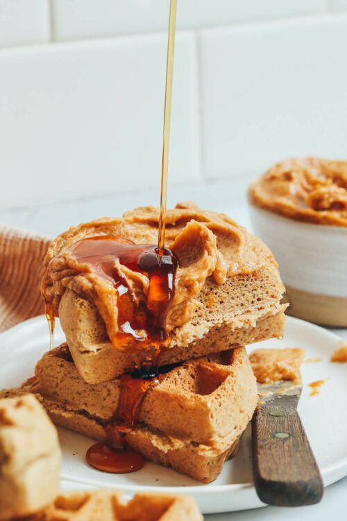 Drizzling maple syrup onto a stack of gluten-free waffles topped with homemade maple butter