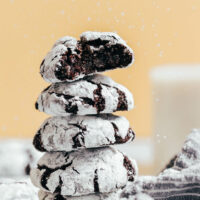 Sprinkling powdered sugar on a stack of gluten-free chocolate crinkle cookies