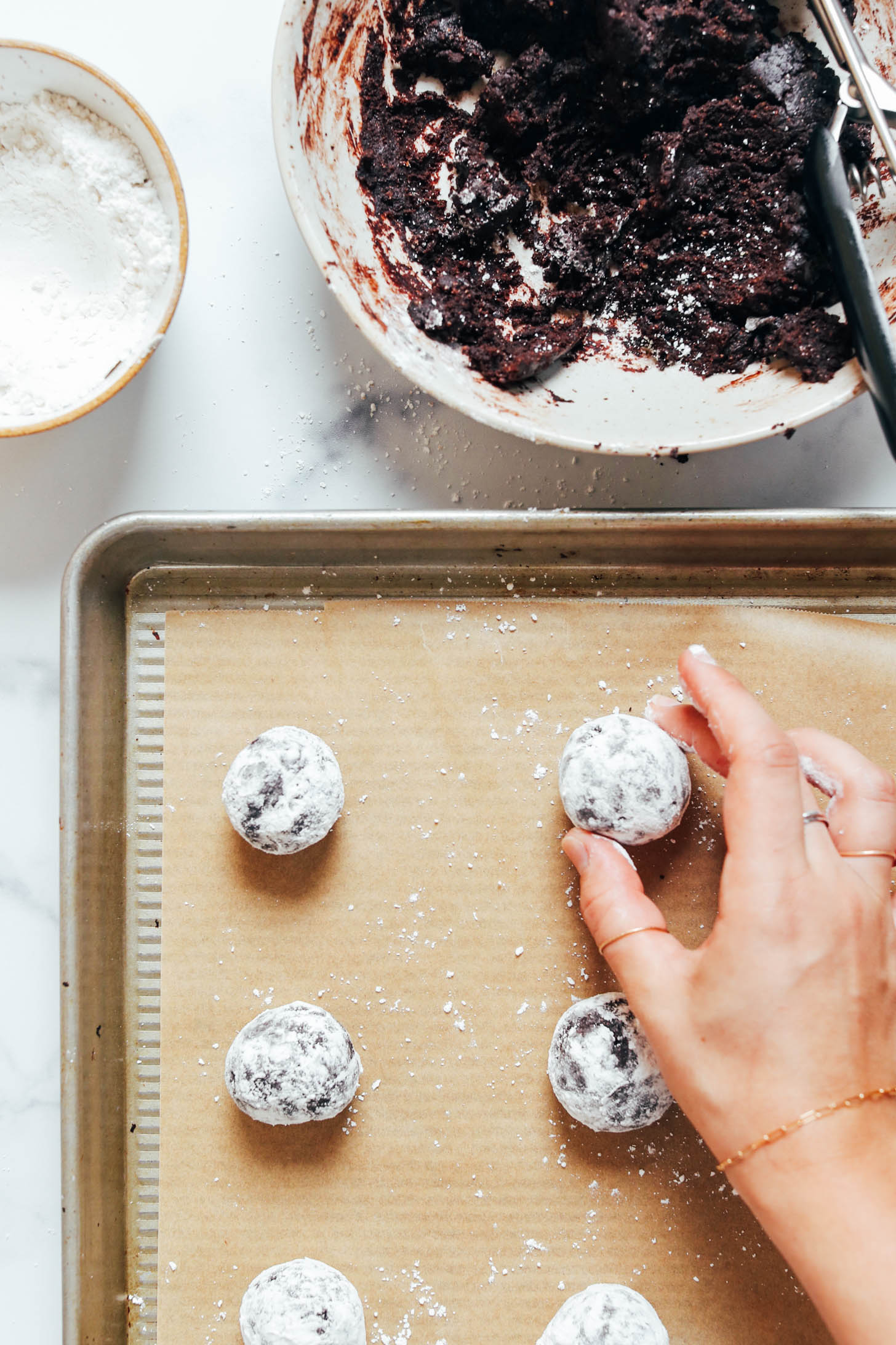 Placing balls of dough coated in powdered sugar onto a parchment-lined baking sheet