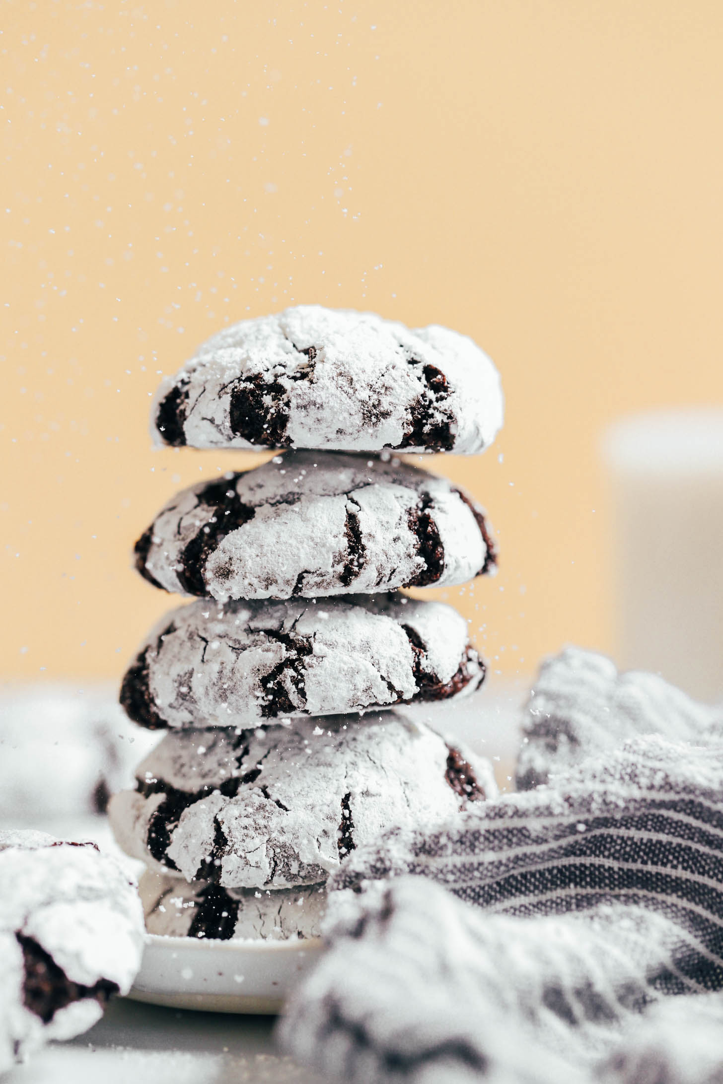 Powdered sugar raining down on a stack of chocolate crinkle cookies