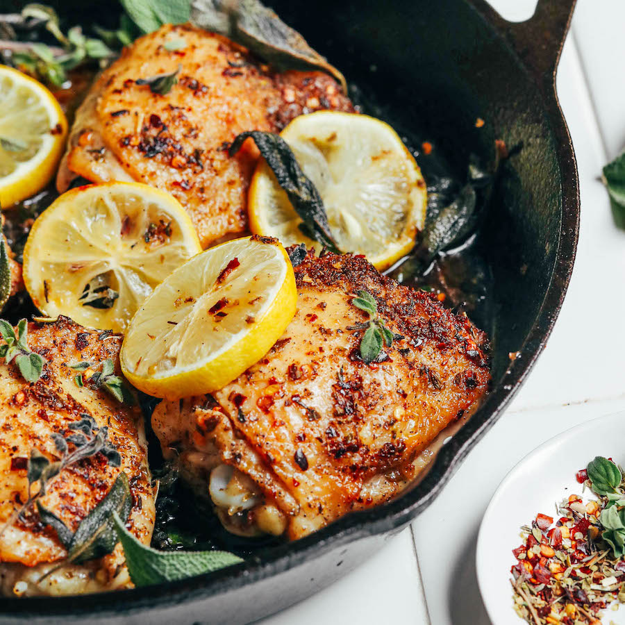 Lemon slices and sage leaves over crispy roasted chicken thighs in a cast iron skillet