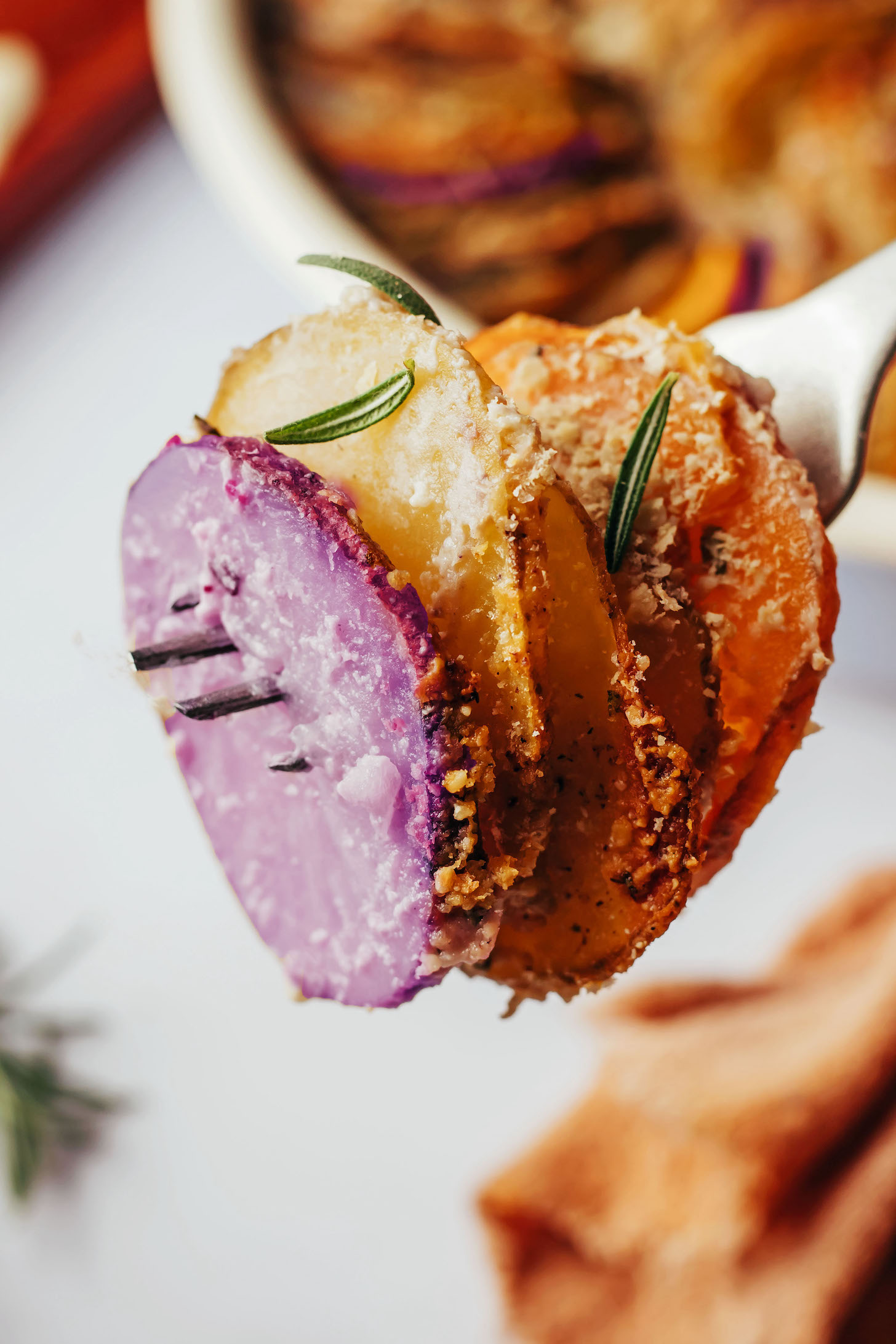 Veganes Kartoffelgratin auf einer Gabel aufgespießt und mit frischem Rosmarin belegt