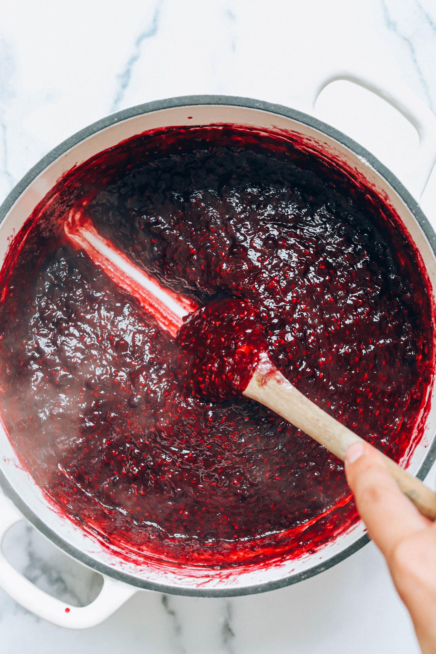 Scraping a spoon across the bottom of a pan to show the thickness of the mixed berry filling