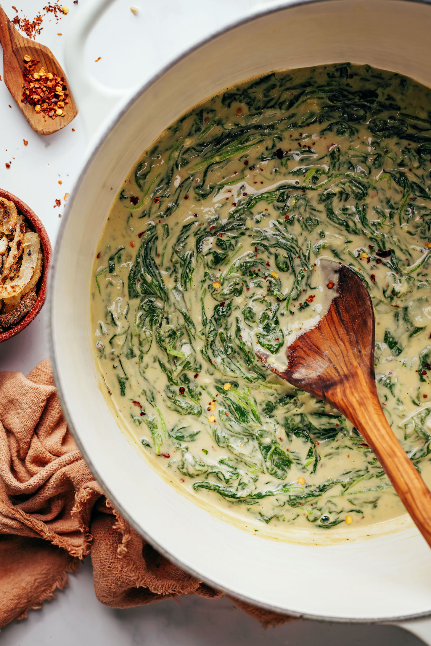 Wooden spoon in a Dutch oven with vegan creamed spinach
