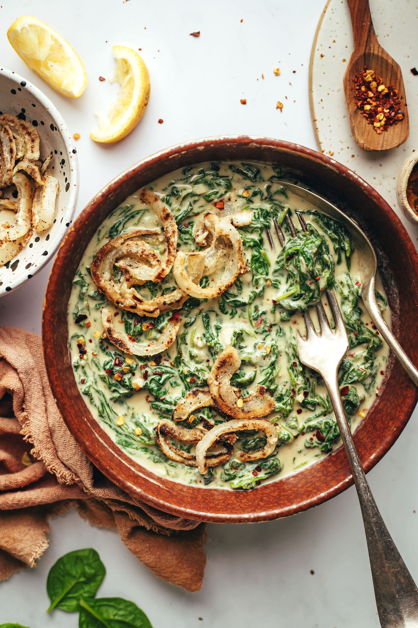Fork and spoon in a bowl of vegan creamed spinach with crispy onions