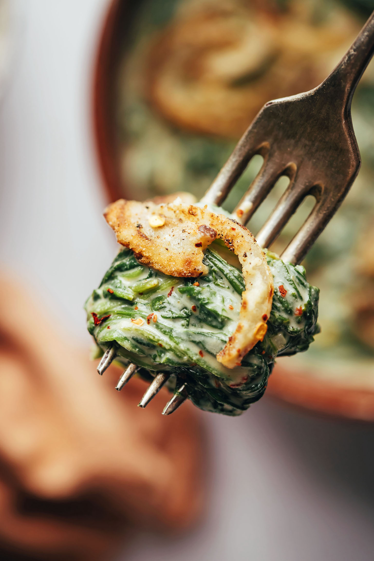 Close up shot of a bite of creamed spinach topped with a crispy fried onion