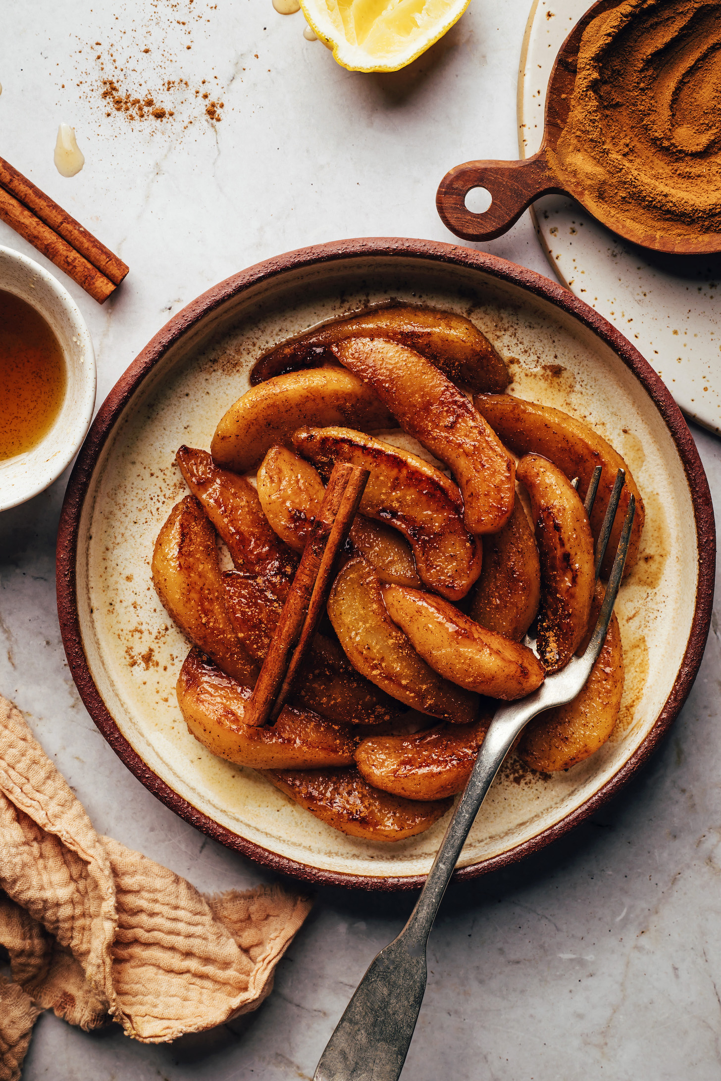 Plate of tender, cinnamon-spiced pears on a plate next to ingredients used to season them