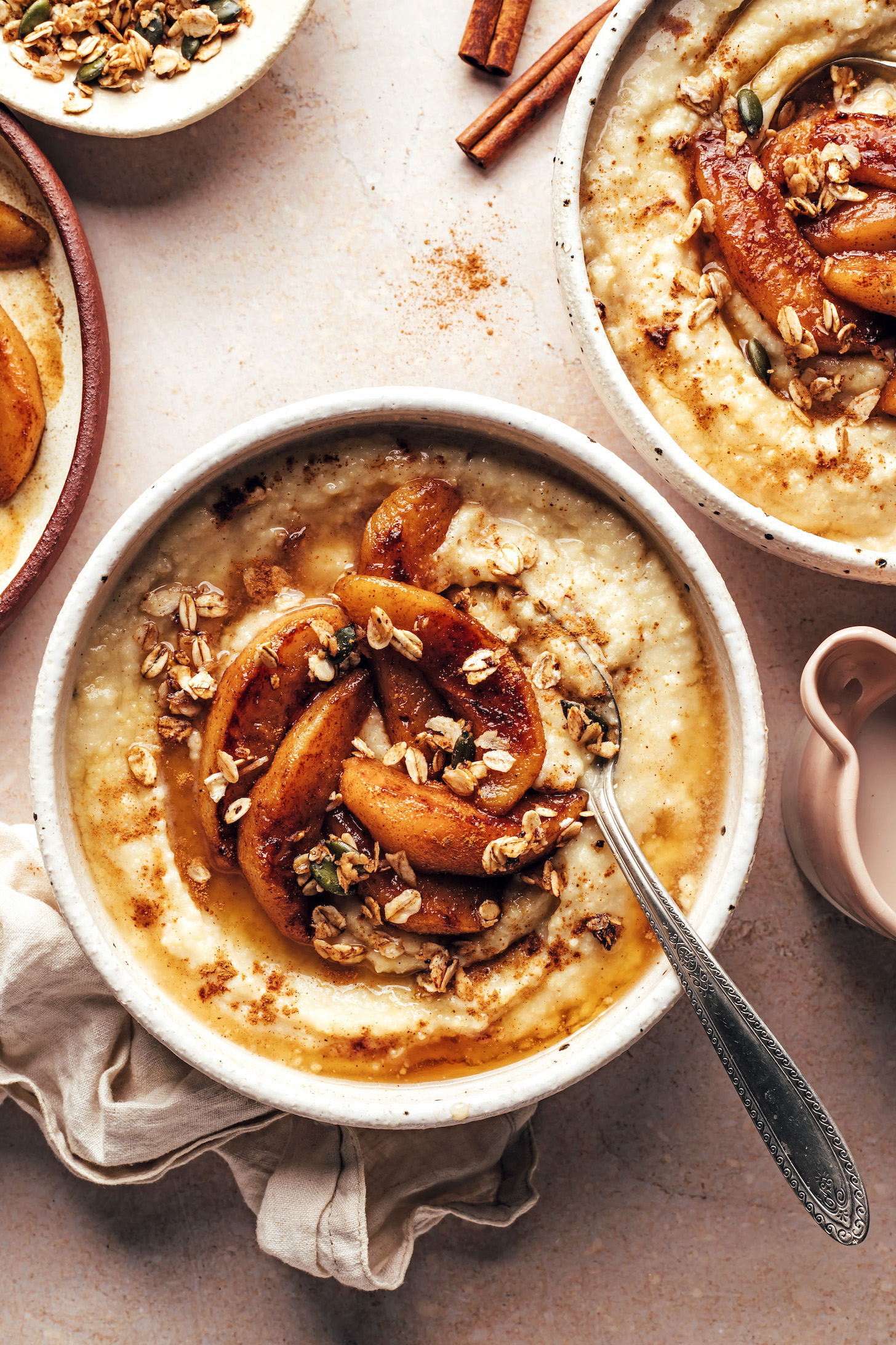 Bowls of millet porridge topped with cinnamon-spiced pears and granola