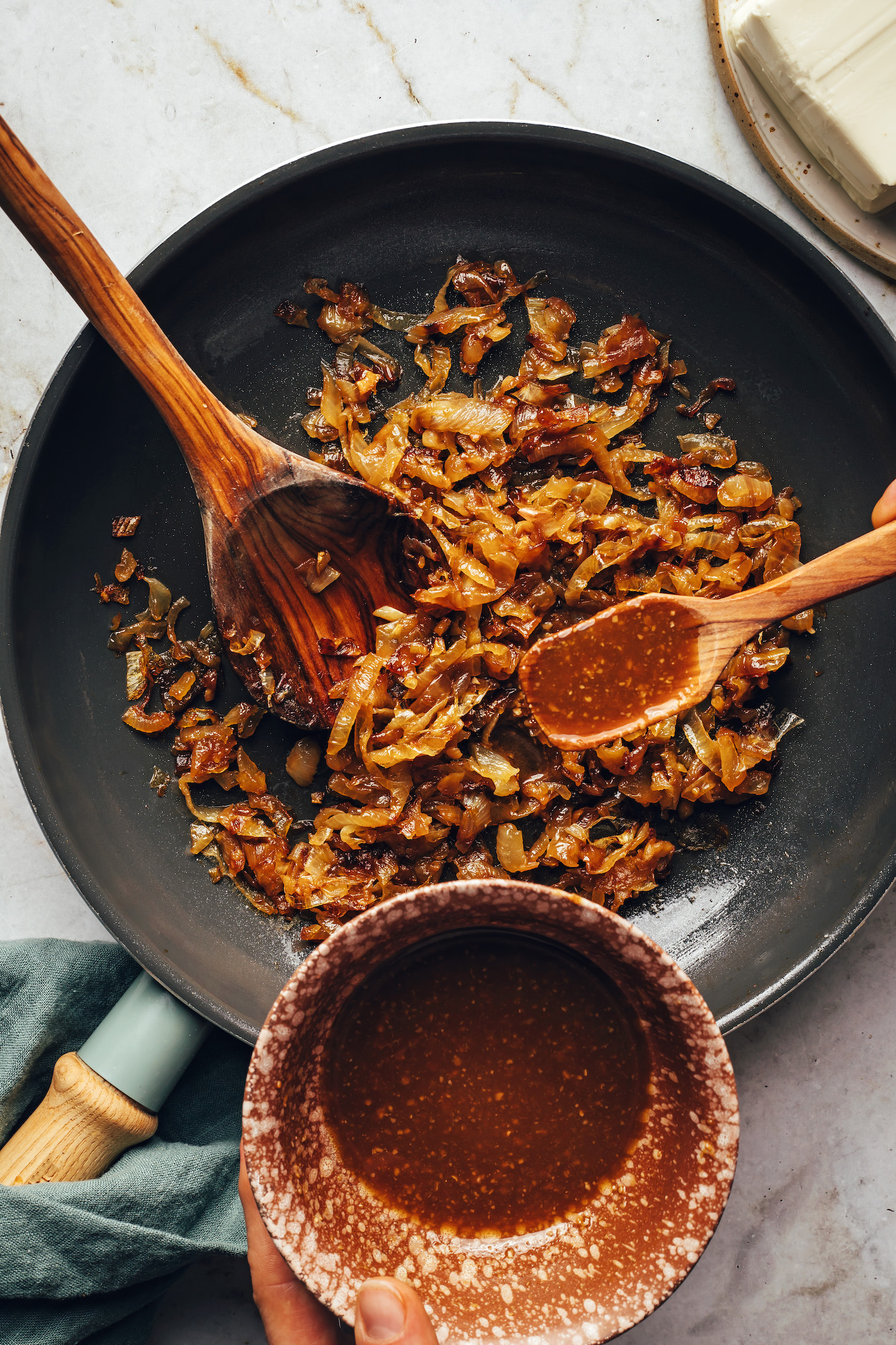 Using a spoon to add a savory, tamari-miso-vinegar sauce to a skillet of caramelized onions