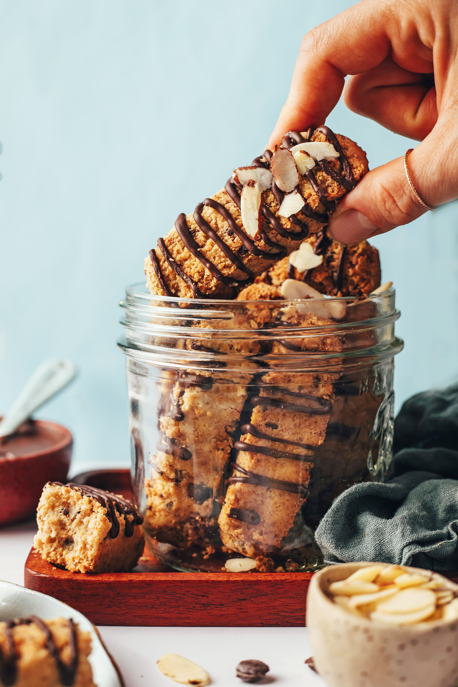 Holding a chocolate-drizzled almond biscotti over a jar with more biscotti