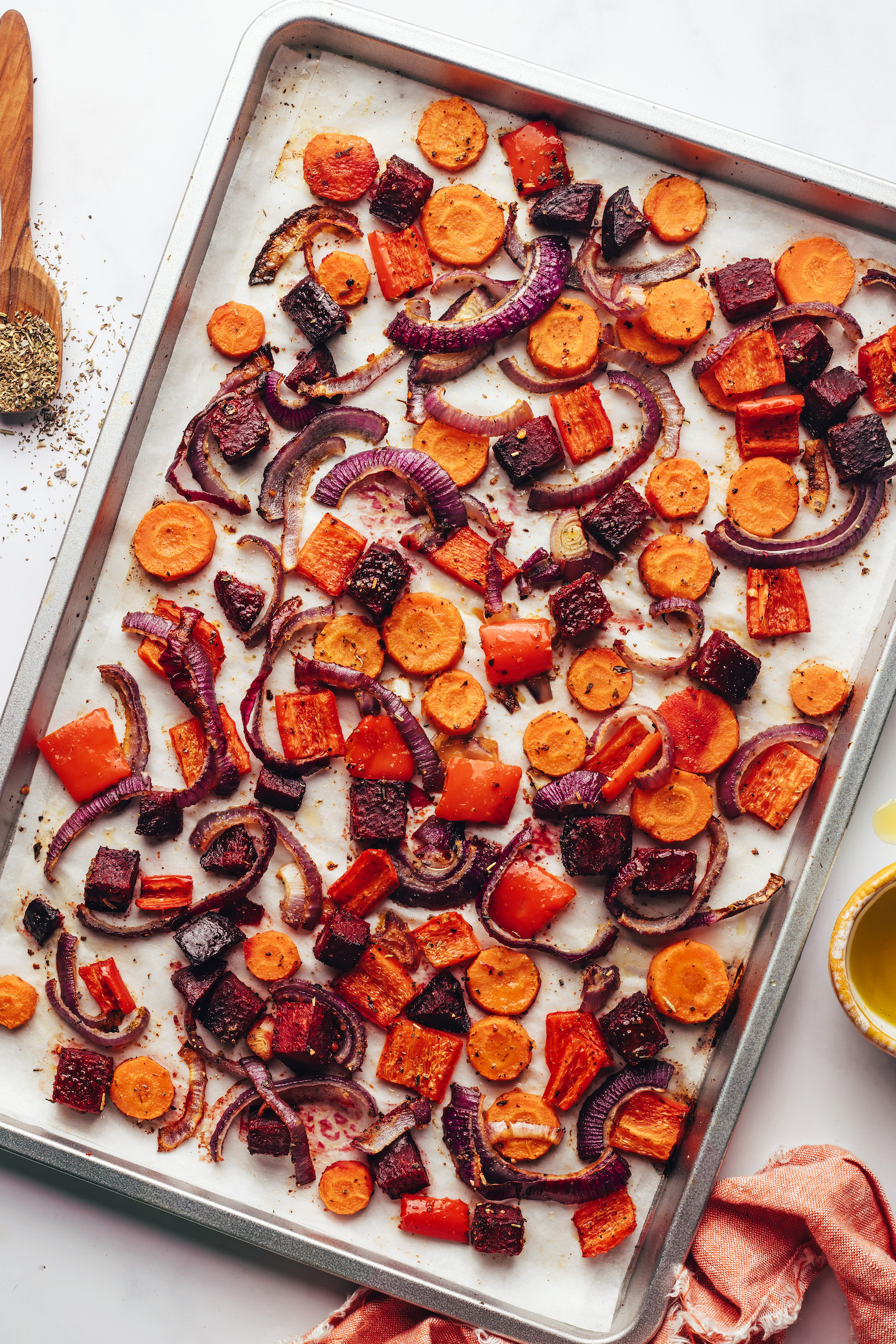 Roasted carrots, beets, red bell pepper, and red onion on a baking sheet