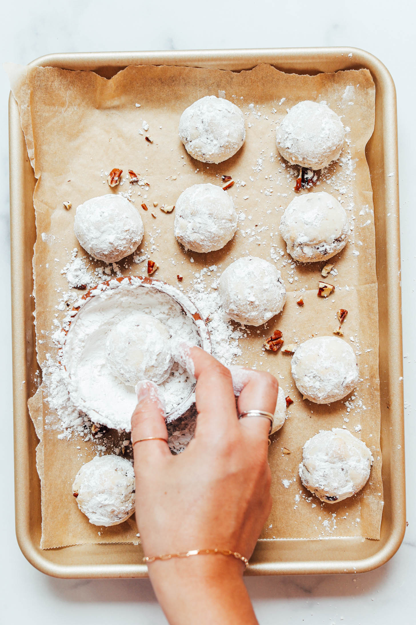 Dipping a freshly baked cookie into a bowl of powdered sugar to make it look like a snowball