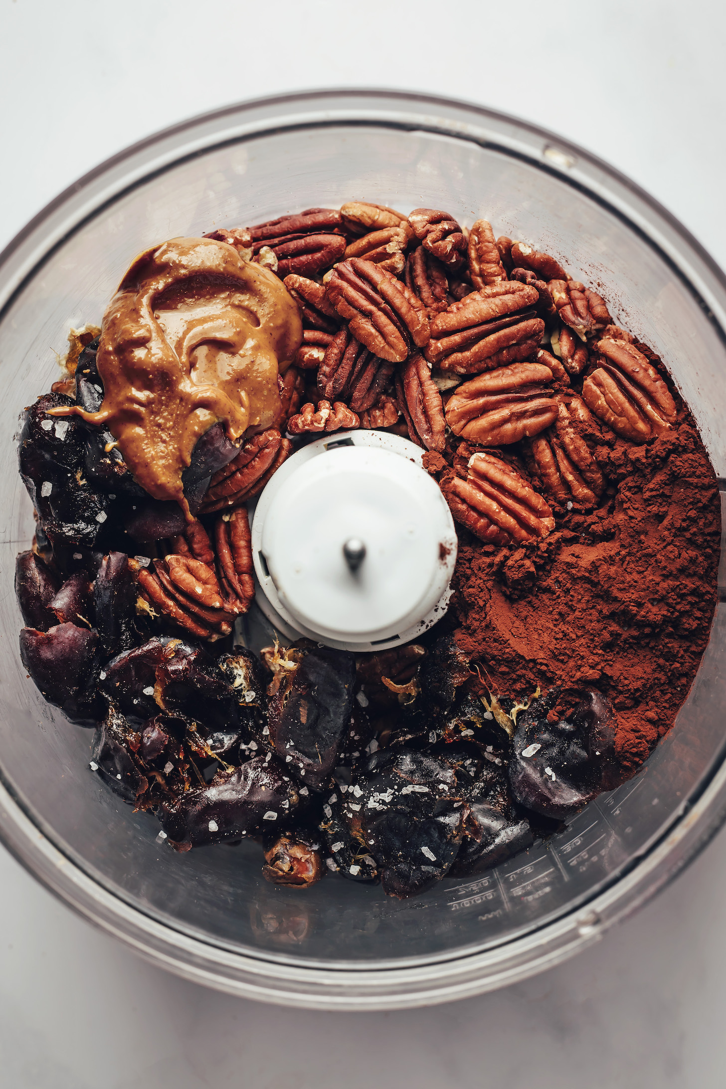 Food processor with pecans, almond butter, dates, salt, and cocoa powder
