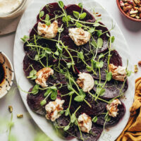 Platter of roasted beet slices with microgreens, balsamic, and vegan goat cheese