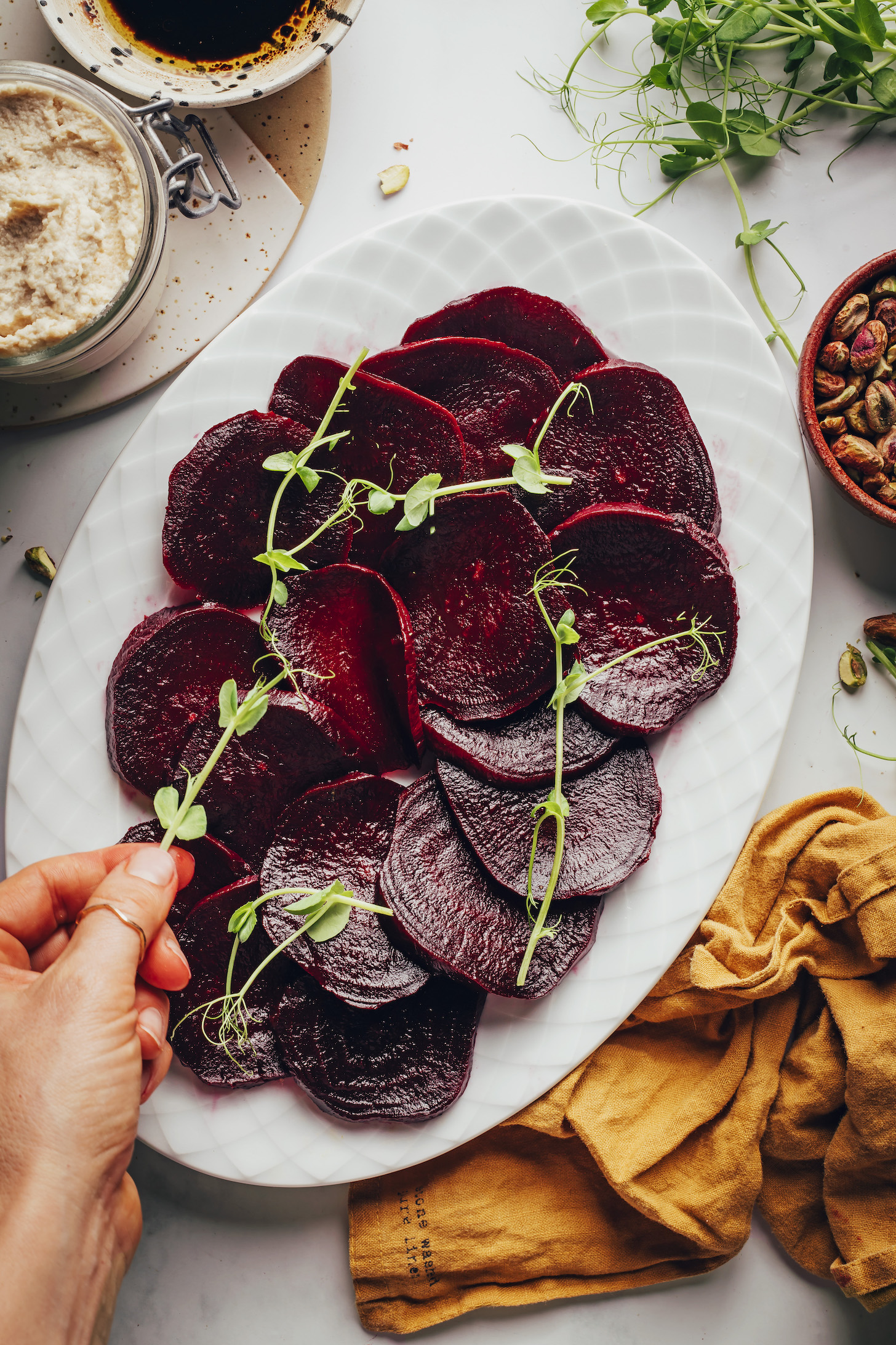 Placing pea shoots onto a platter of sliced roasted beets