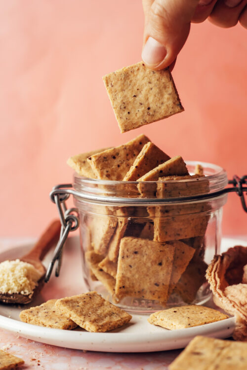 Holding a grain-free almond flour cracker above a jar with more crackers