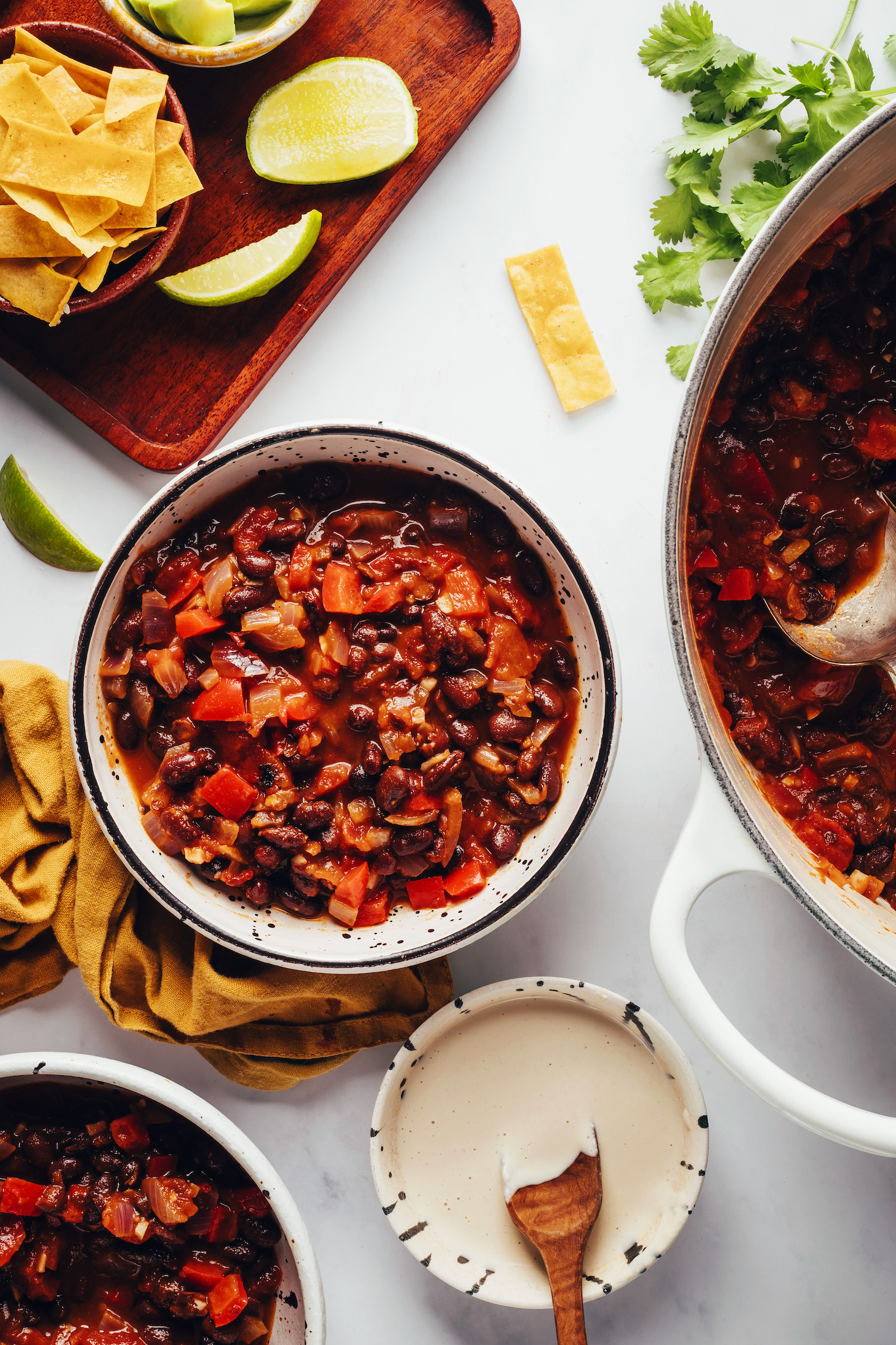 Bowls and Dutch oven of chipotle black bean chili next to toppings