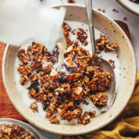 Pouring dairy-free milk into a bowl of buckwheat granola