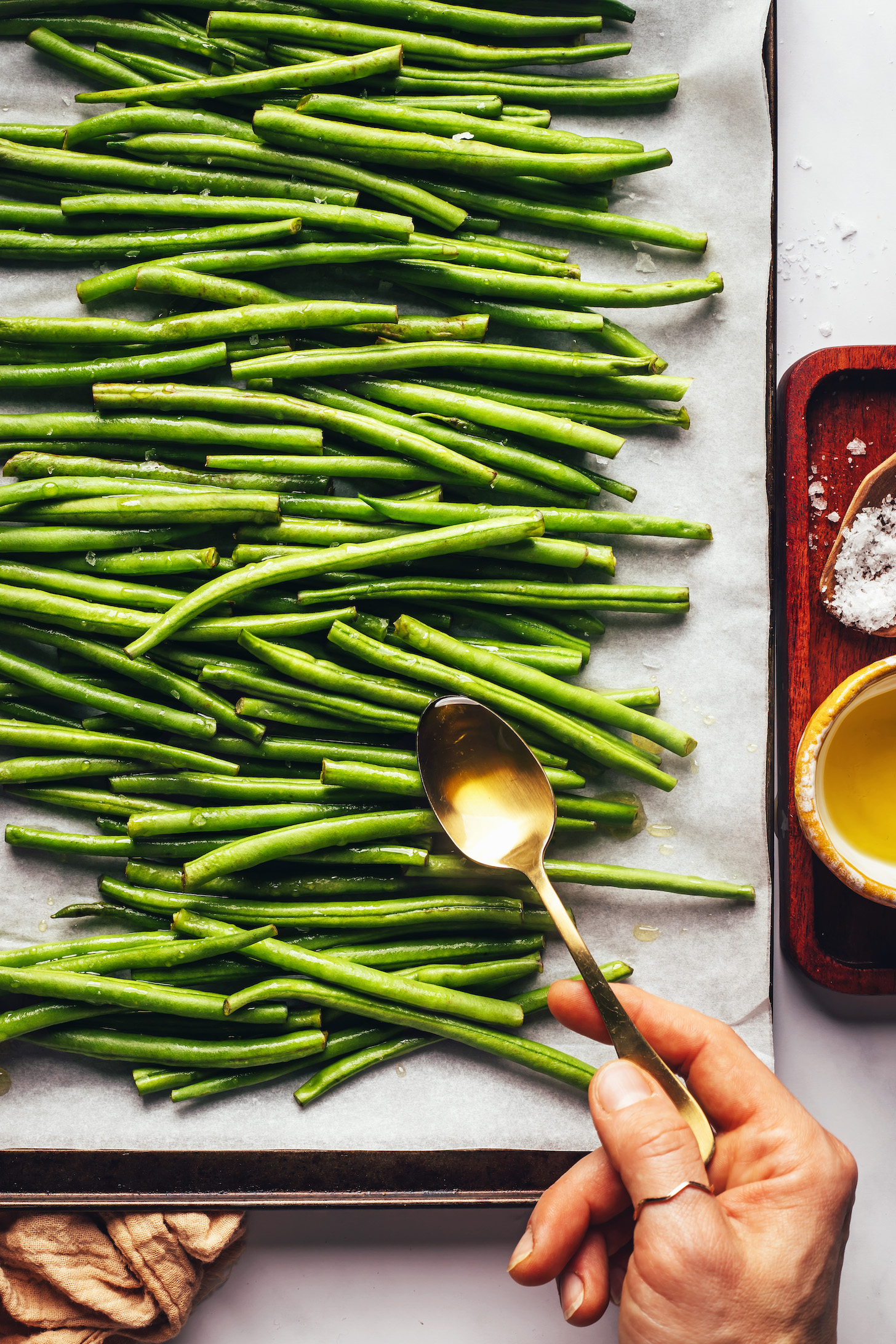 Use a spoon to drizzle olive oil over green beans on a baking sheet