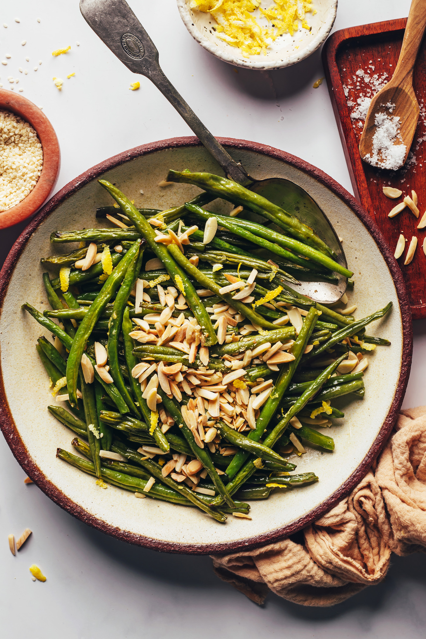 A bowl of roasted green beans with lemon zest, sesame seeds, salt, and chopped almonds.