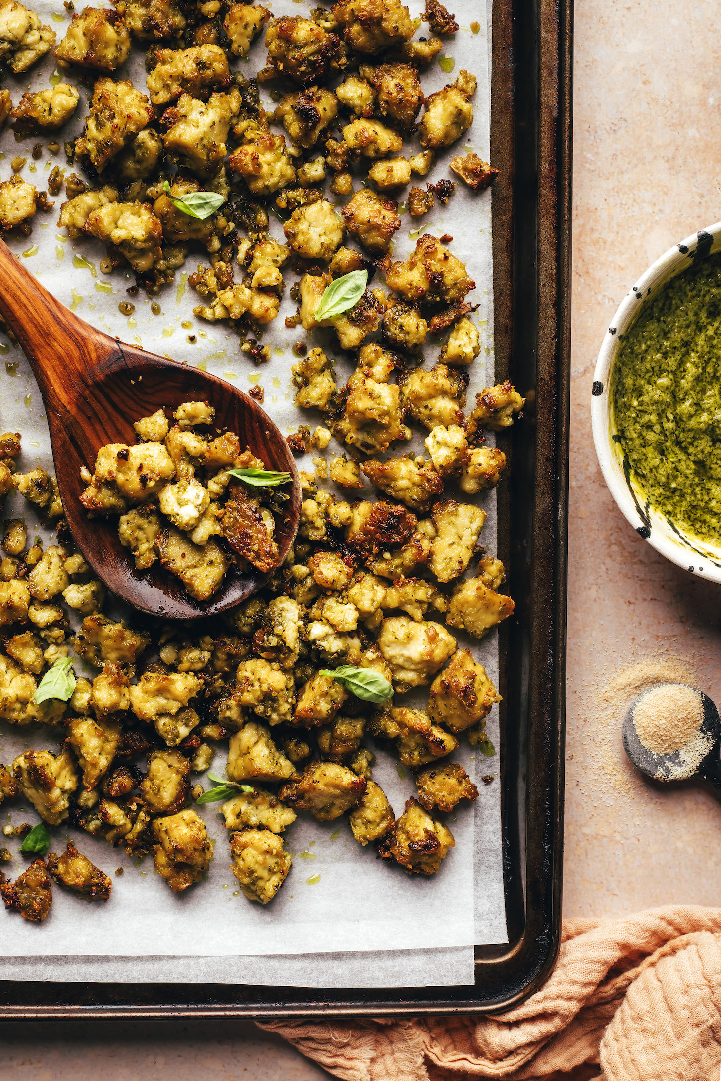 Pesto next to a parchment-lined baking sheet of crispy baked tofu with pesto