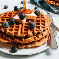 Drizzling maple syrup onto a stack of protein waffles
