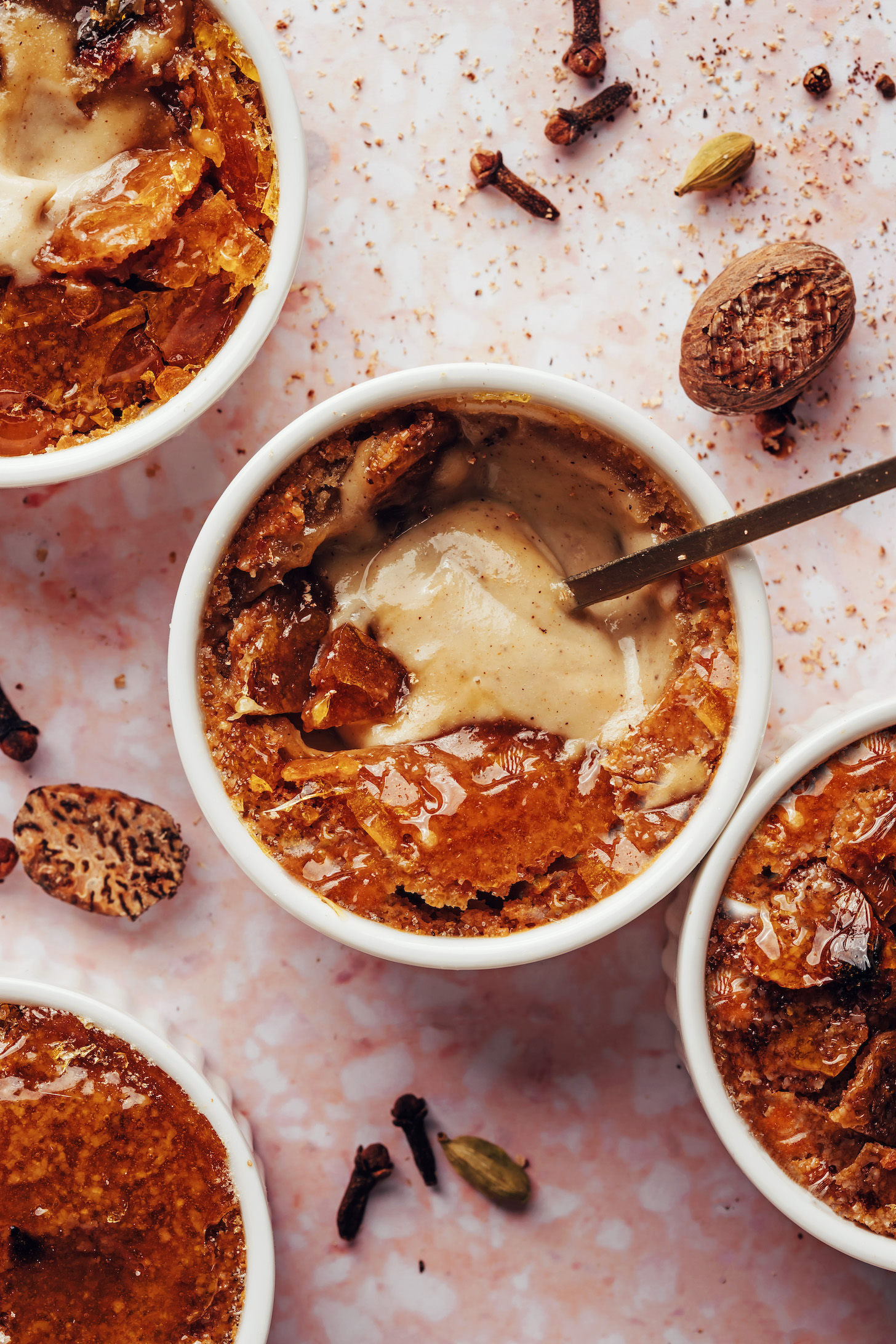 Nutmeg, cardamom, and cloves next to bowls of vegan chai-spiced creme brulee