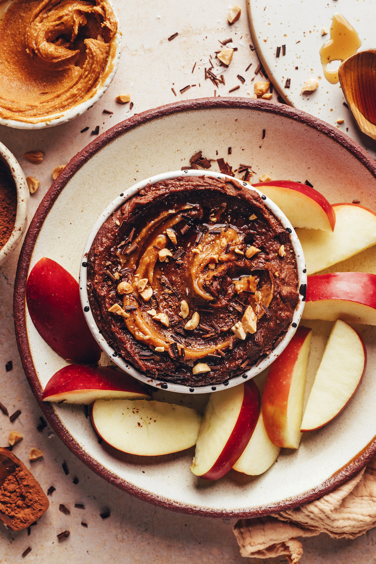 Sliced apples around a bowl of chocolate hummus with a peanut butter swirl