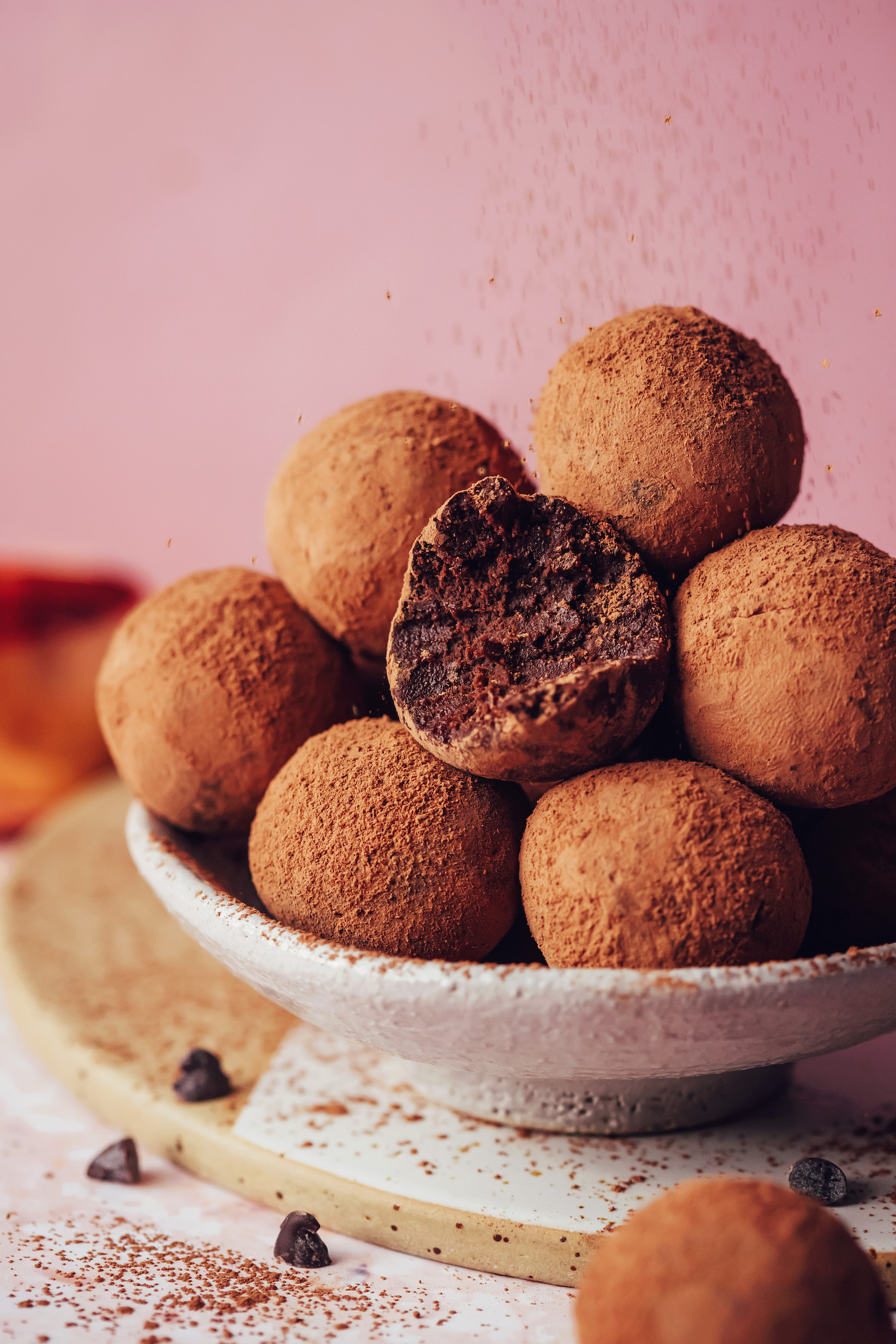 Посыпьте какао-порошком миску с трюфелями из сладкого картофеля из темного шоколада.