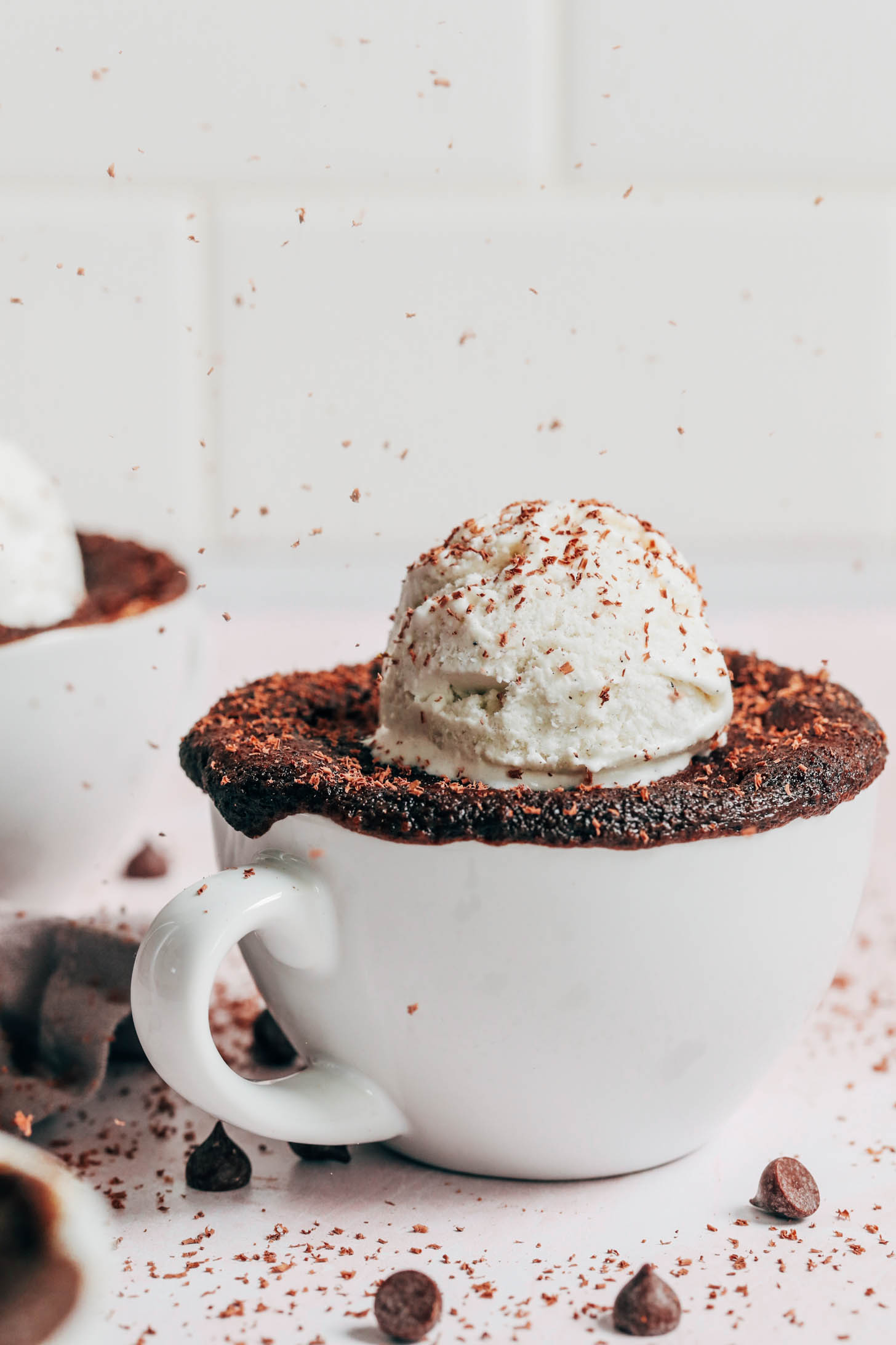 Shaved dark chocolate falling onto a scoop of vanilla ice cream on a chocolate mug cake