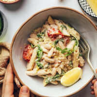 Hands holding a bowl of lemon garlic pasta with white beans and arugula