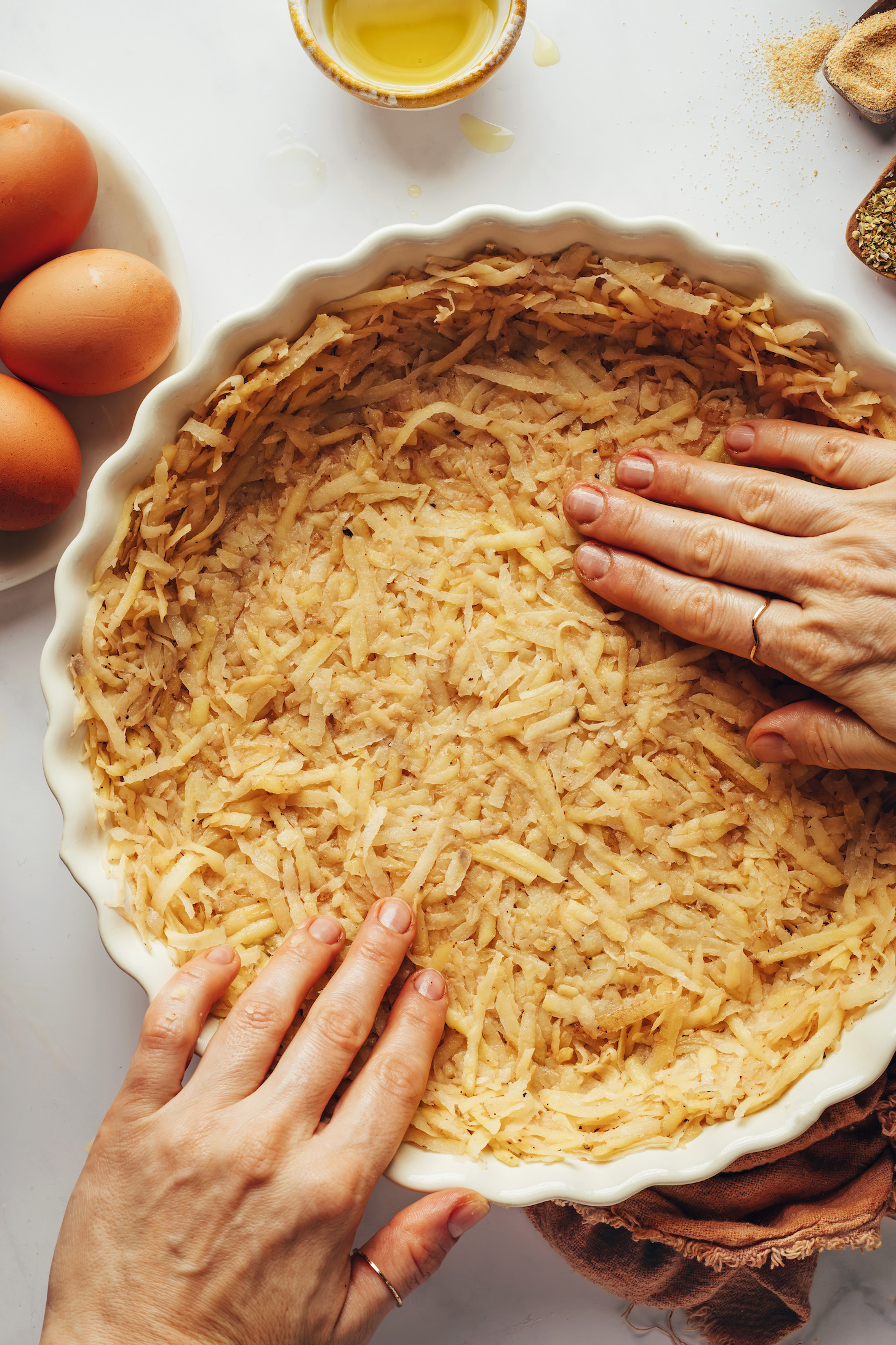 Shredded potatoes are required for a potato crust quiche. Yukon gold retains its color better than russet, which grays more rapidly, thus we prefer them. We mix the potatoes with olive oil, salt, and pepper before pressing them equally into a pie pan after pressing the extra moisture from the potatoes.