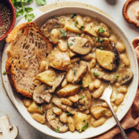 Crusty sliced bread in a bowl of white bean mushroom stew