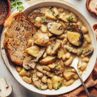 Spoon in a bowl of white bean mushroom stew with a slice of crusty bread