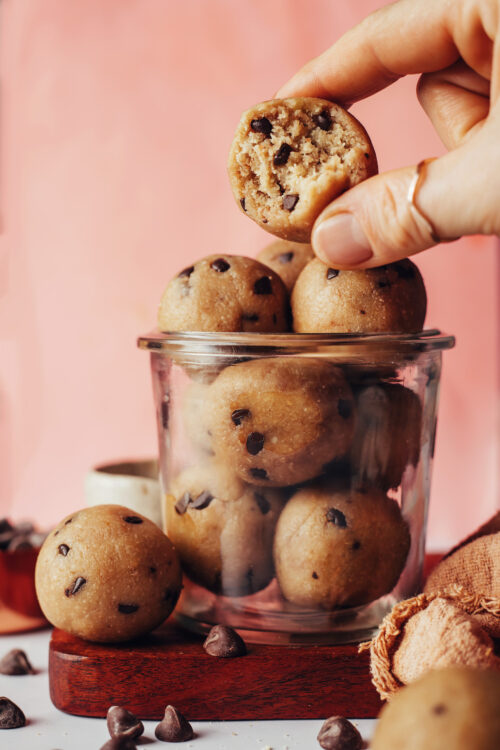 Holding an edible chocolate chip cookie dough bite above a jar of more bites