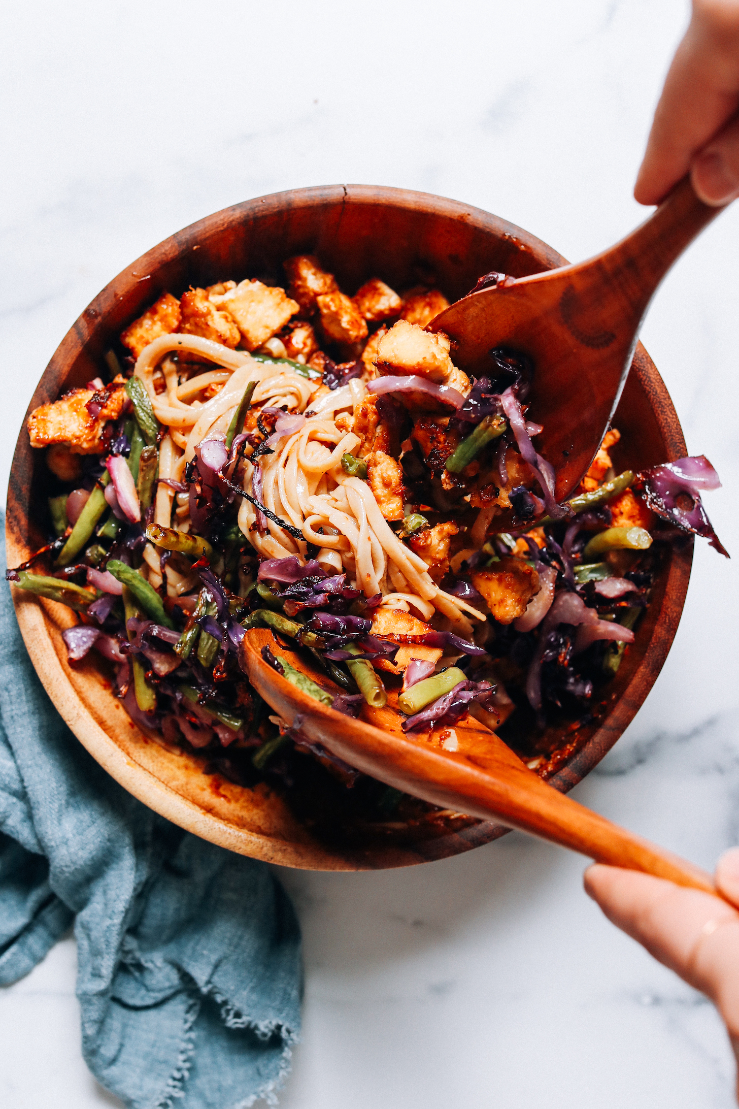 Using wooden salad spoons to toss ginger sesame noodles with baked crispy tofu and veggies
