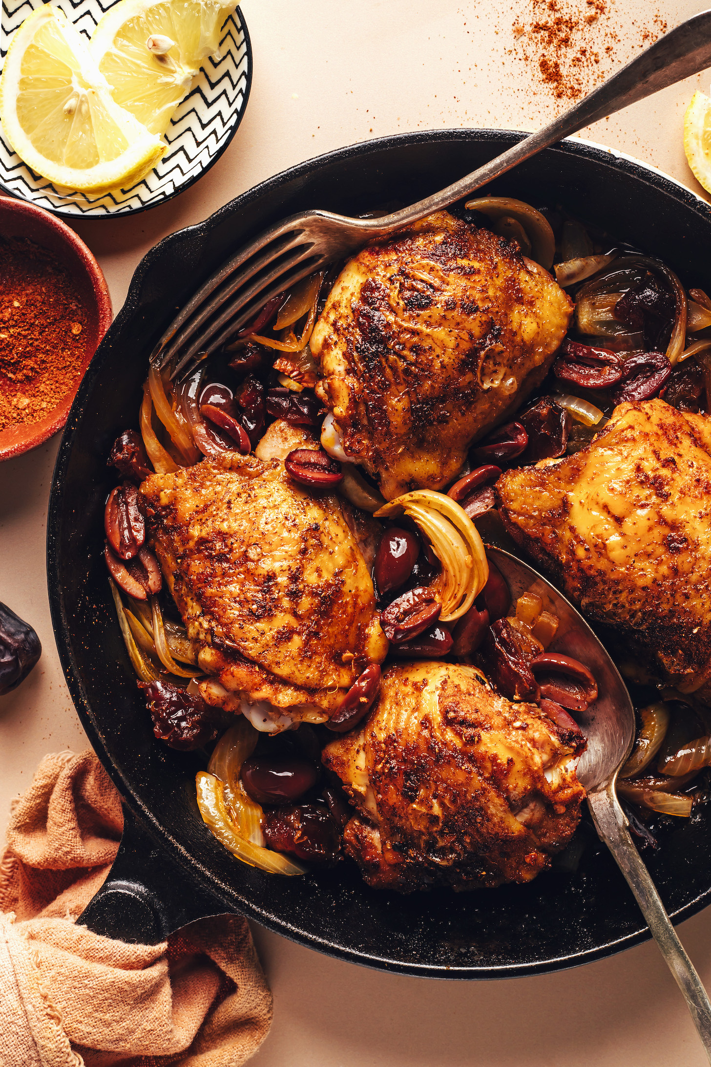 Cast iron skillet of crispy baked Mediterranean chicken thighs with olives, dates, and onions