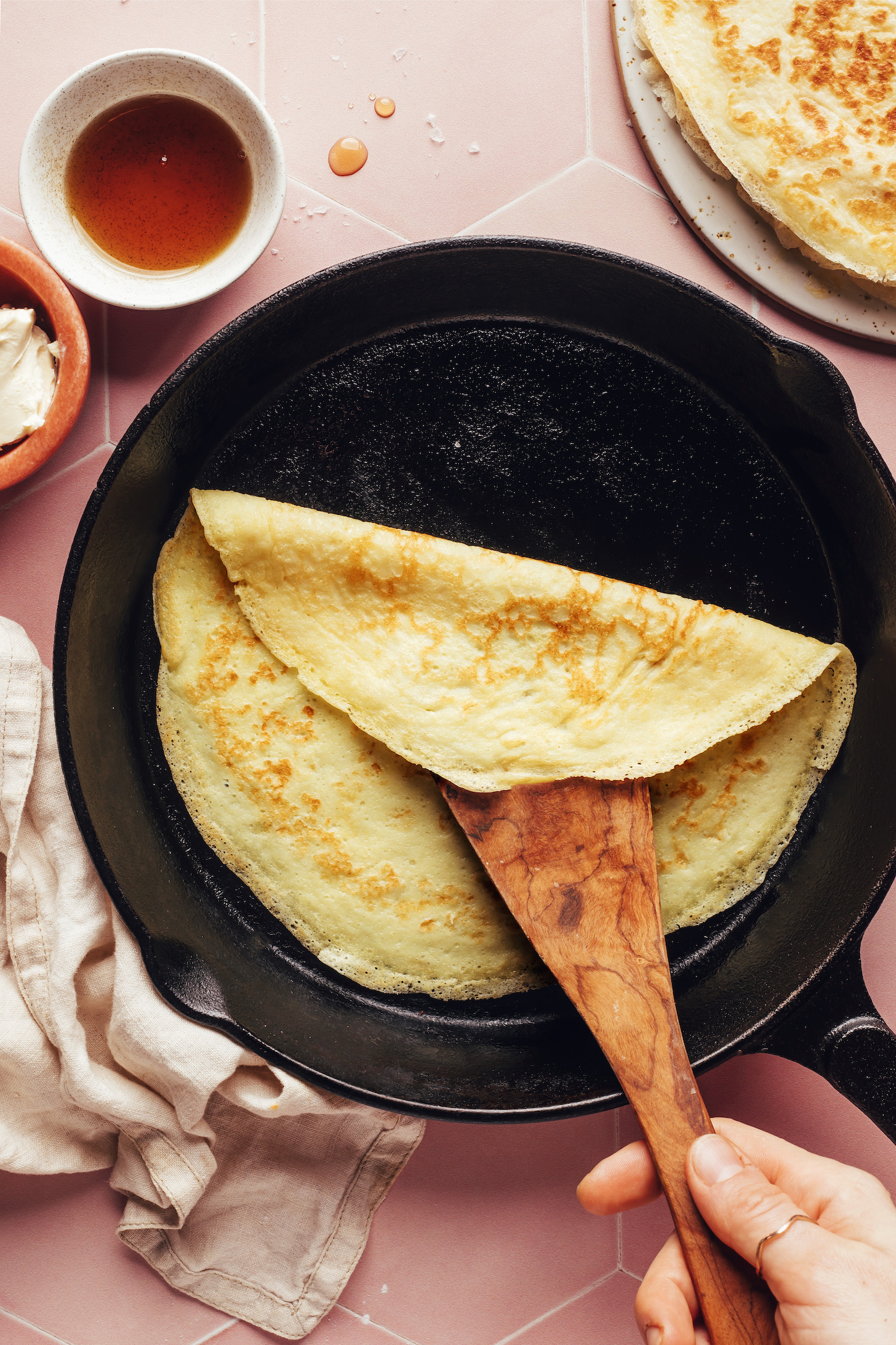 Using a wooden spoon to show the golden brown underside of a crepe in a cast iron skillet