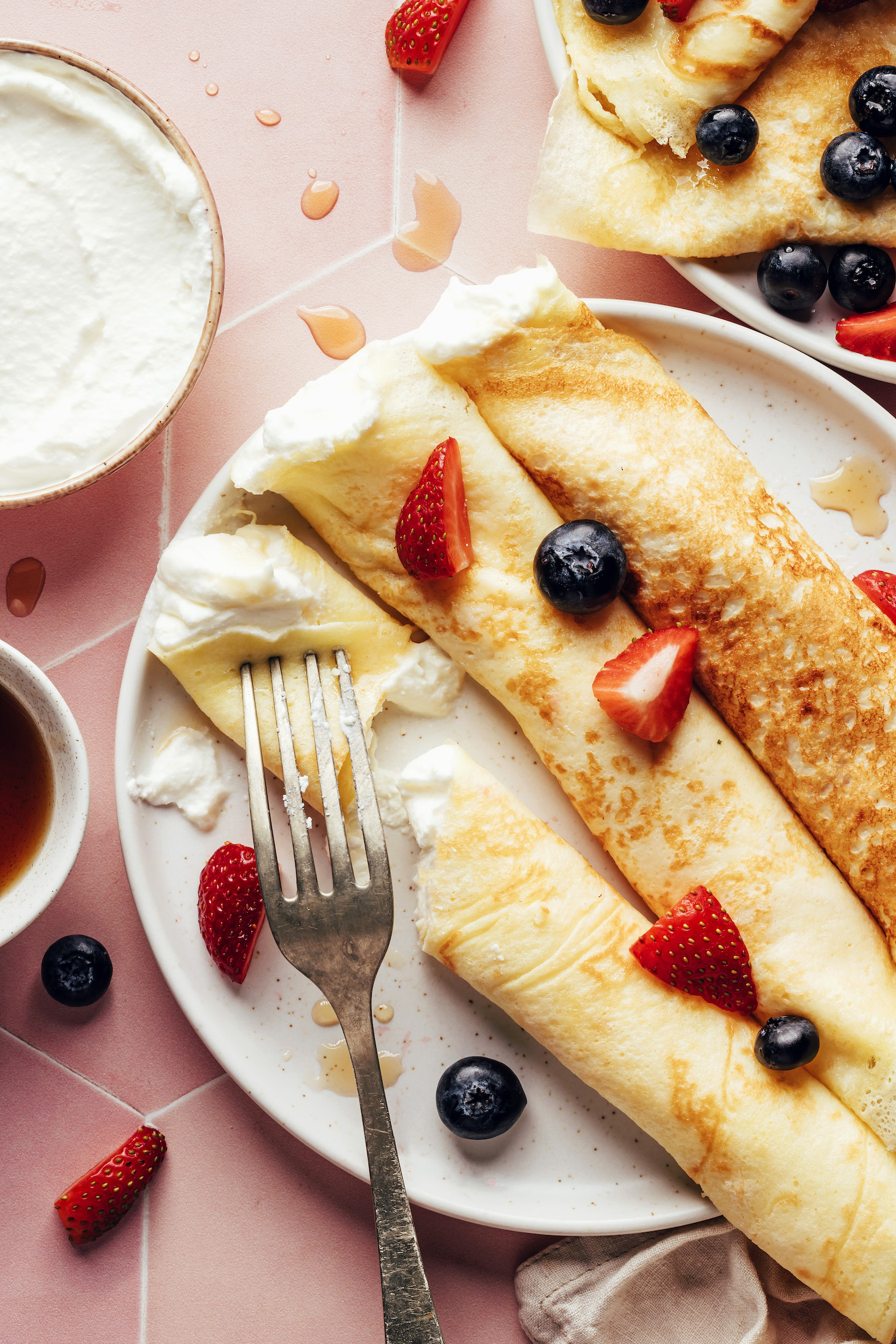 Plate of rolled up gluten-free crepes filled with coconut whipped cream and topped with berries