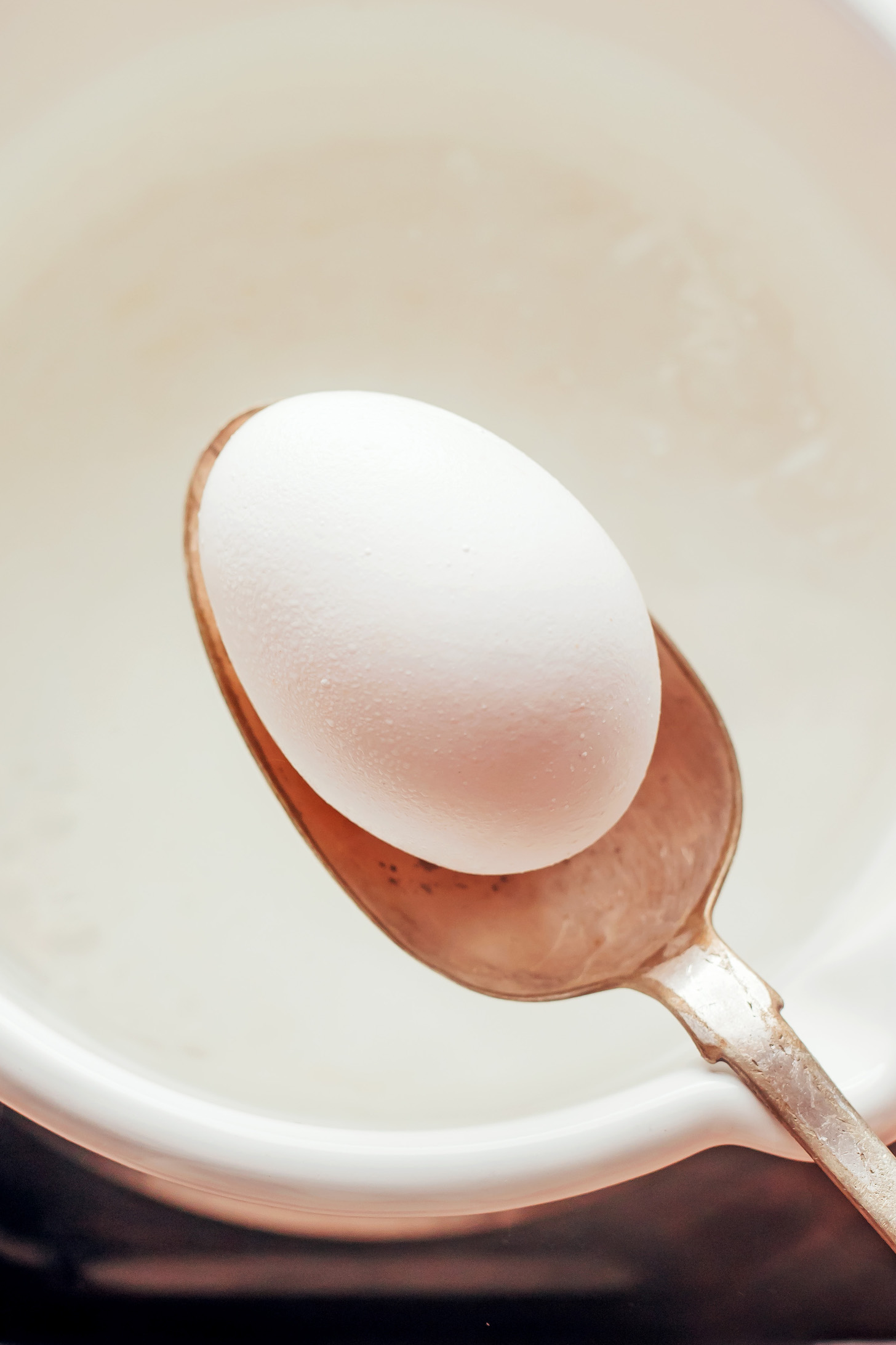 Using a spoon to lower an egg into a pot of water